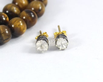 May include: A pair of silver stud earrings with a clear round gemstone set in a black bezel. The earrings have a gold post.