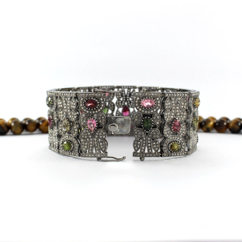 May include: A silver bracelet with a floral design and colorful gemstones. The bracelet is open and has a clasp.