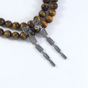 May include: A pair of silver dangle earrings with a geometric design. Each earring features five rectangular shapes with a textured surface. The earrings are hanging from a tiger's eye beaded necklace.