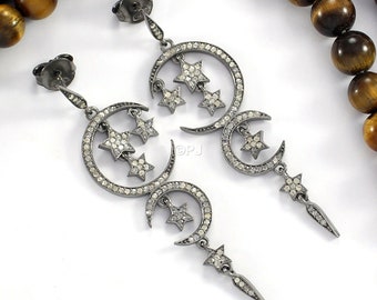 May include: A pair of silver dangle earrings with a crescent moon design and a star pendant. The earrings are adorned with small, clear stones.