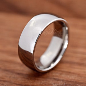 May include: A polished silver-toned metal ring with a smooth, domed surface and a rounded profile. The band features a high-gloss, reflective finish that catches the light, creating a clean and simple appearance. The text TrendyRing is visible.