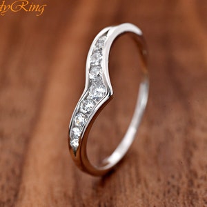 May include: A silver-toned curved ring featuring a channel setting with seven clear, round-cut stones arranged in a wave pattern. The metal band has a polished finish. The text "TrendyRing" is visible in the upper left corner of the image.