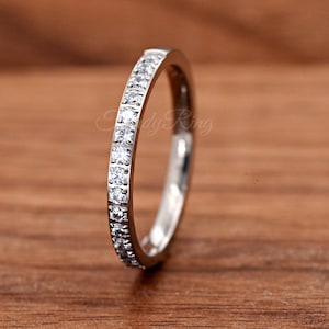 May include: A silver-toned metal band ring featuring a row of small, clear, round-cut stones set along the outer edge. The ring has a polished finish and a slim profile, with the text "Candy Ring" visible in a faint, cursive font on the metal surface.