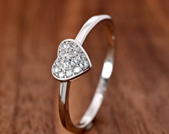 May include: A silver-toned ring featuring a heart-shaped centerpiece adorned with multiple small, clear, sparkling stones. The band is smooth and polished, and the text "TrendyRing" is visible in the upper left corner of the image.