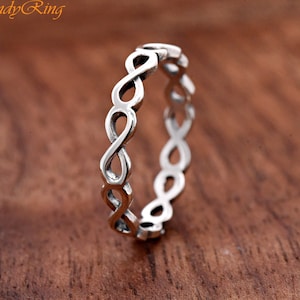 May include: A silver-colored ring featuring a continuous band of interconnected infinity symbols. The metal has a polished finish with darkened recessed areas to highlight the repeating figure-eight pattern. The text TrendyRing is visible.