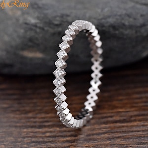 May include: A silver band ring with a row of small, clear cubic zirconia stones set in a chevron pattern.