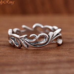 May include: A silver ring with a delicate, intricate design featuring swirling, floral-like patterns.
