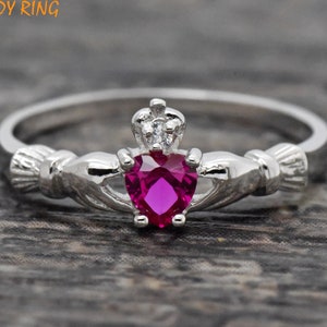 May include: A silver Claddagh ring with a pink heart-shaped gemstone and a small crown with a clear stone on top.