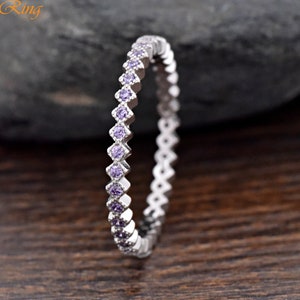 May include: A silver ring with a continuous row of small, square-cut purple gemstones. The ring is set against a dark, textured background, with the brand name "Trendy Ring" visible in the upper left corner.