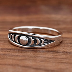 May include: A silver ring with a crescent moon design. The ring has a smooth, polished finish and features a series of crescent moons encircling a full moon.