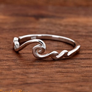 May include: A silver ring with a wave design. The wave is stylized and has a swirl at the top.