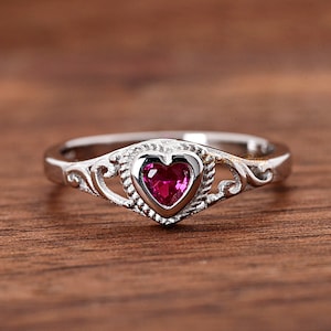 May include: A silver ring with a heart-shaped pink gemstone set in a decorative filigree design.