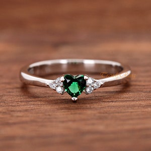 May include: A silver ring with a green heart-shaped gemstone and smaller clear gemstones on the band.