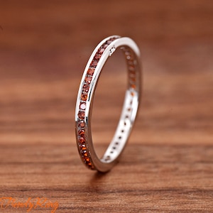 May include: A silver band ring with a row of small orange gemstones around the entire band.