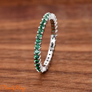 May include: A silver band ring with a row of small, green gemstones around the entire band.