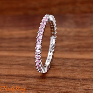 May include: A silver band ring with a row of small pink gemstones around the entire band.