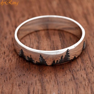 Puede incluir: Un anillo de banda de plata con una silueta de un bosque grabado en la superficie.