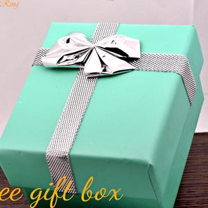May include: A square turquoise gift box featuring a silver metallic bow and a silver textured ribbon wrapped around the lid. The text TrendyRing is visible in the top left corner, and the text free gift box is written in yellow at the bottom.