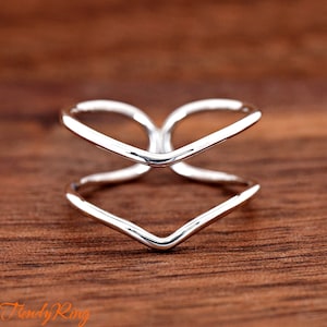 May include: A silver ring with a double V-shaped design. The ring is made of a smooth, polished metal and has a simple, modern style.