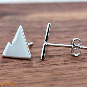 May include: A pair of silver mountain-shaped stud earrings. The earrings are made of a smooth, shiny metal and have a simple, minimalist design.