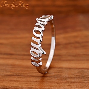 May include: A silver-toned metal ring featuring the word Aquarius in a cursive script font as the centerpiece. The band is thin and polished, with the text extending vertically along the finger. The text Trendy Ring is visible in the top left corner.