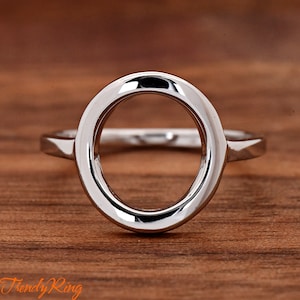 May include: A silver ring with a large, round, open circle design. The ring is on a wooden surface.