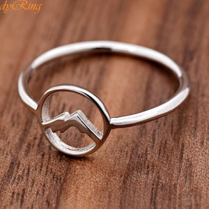 May include: A silver ring with a mountain range design inside a circle.
