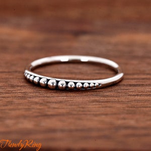 May include: A silver ring with a row of small, round beads along the band.