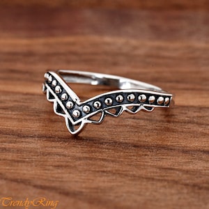 May include: A silver ring with a V-shaped design and a beaded edge.