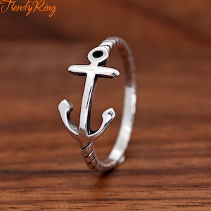 May include: A silver-toned metal ring featuring a prominent anchor design as the centerpiece. The band of the ring displays a subtle rope-like texture pattern. The text "Trendy Ring" is visible in the upper left corner of the image.