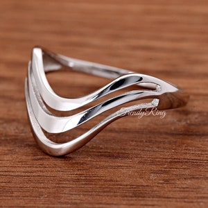 May include: A polished silver-toned ring featuring a V-shaped chevron design with three distinct, parallel bands that curve upward. The metal surface is smooth and reflective, and the text "Trendy Ring" is printed in a script font on the side.