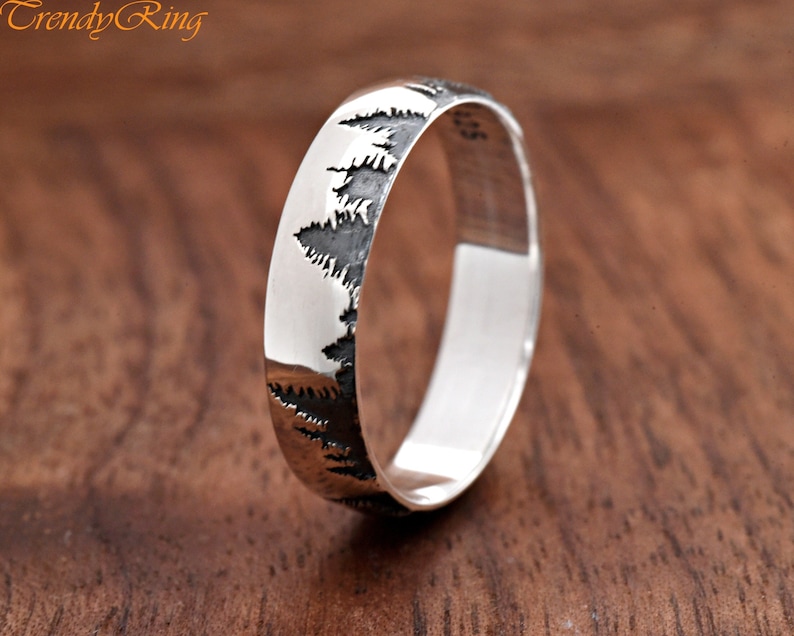 May include: A silver band ring with a design of a row of pine trees etched into the side.