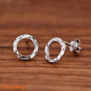 May include: A pair of silver circle stud earrings with a textured, faceted design. The earrings have a simple post and butterfly back.