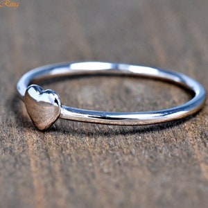 May include: A polished silver-toned ring featuring a small, smooth heart-shaped charm attached to a thin, circular band. The text "TrendyRing" is visible in the upper left corner of the image, presented in a simple, orange-colored font.