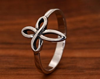 May include: A silver-toned metal ring featuring a four-petaled, open-work floral or butterfly-shaped design element on the front. The band is smooth and polished, with darkened recessed areas within the central motif. The text Trendy Ring is visible.