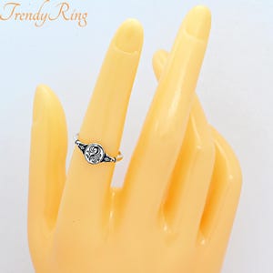 May include: A silver-coloured ring featuring a small, oval-shaped face with an intricate black engraved swirl pattern. The band is thin and metallic, and the text Trendy Ring is visible in the upper left corner of the image.