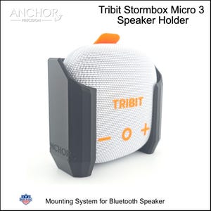 May include: A dark grey plastic speaker holder for a Tribit Stormbox Micro 3 Bluetooth speaker. The holder features the embossed text ANCHOR on the side. The white speaker has orange controls including a plus, minus, and circle symbol.