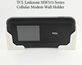 May include: A white wall mount for a TCL Linkzone MW513 series cellular modem. The modem is black with a screen and the TCL logo.