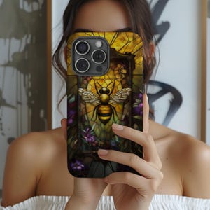 May include: A black phone case with a stained glass design featuring a bee and flowers. The case has a cutout for the phone's camera lens.