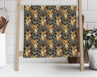 May include: A decorative kitchen towel featuring a repeating pattern of foxes amidst floral elements. The foxes have orange fur and are set against a dark blue background with yellow and white flowers. The towel is displayed on a wooden ladder-style rack.