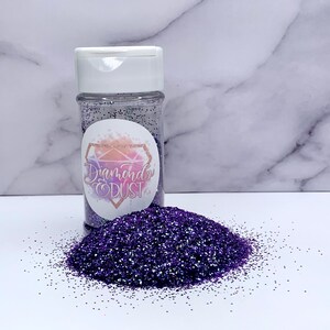 May include: A clear plastic jar filled with purple glitter with a white lid. The jar has a label that says "Diamond Dust".
