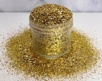 May include: A clear jar filled with gold glitter. The glitter is loose and has a variety of sizes. The jar is sitting on a white surface.