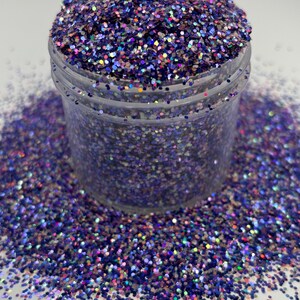 May include: A clear plastic jar filled with iridescent purple glitter. The glitter is scattered around the jar on a white surface. The glitter has a mix of colors, including blue, pink, and green, creating a shimmering effect. Ideal for crafts.
