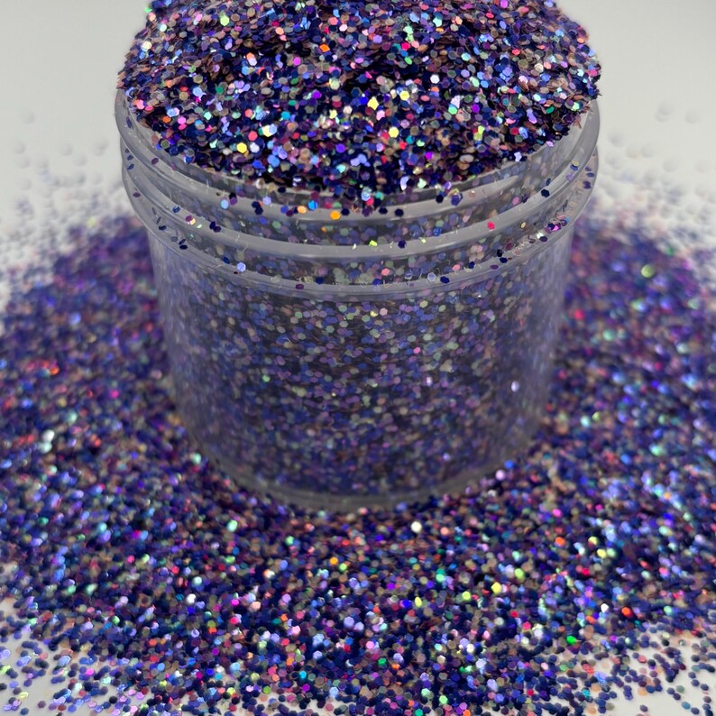 May include: A clear plastic jar filled with iridescent purple glitter. The glitter is scattered around the jar on a white surface. The glitter has a mix of colors, including blue, pink, and green, creating a shimmering effect. Ideal for crafts.