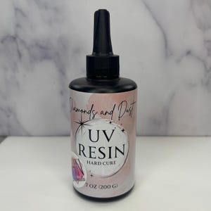 May include: A black bottle of UV resin with a black nozzle. The label reads "Diamonds and Dust" and "UV RESIN HARD CURE". The bottle contains 7 oz (200 g) of resin. The background is a marble pattern.