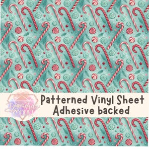 Könnte beinhalten: Eine gemusterte Vinylfolie mit einem sich wiederholenden Design aus rot-weißen Zuckerstangen, Pfefferminzbonbons und Zweigen auf hellblauem Hintergrund. Der Text "Patterned Vinyl Sheet Adhesive backed" wird angezeigt.