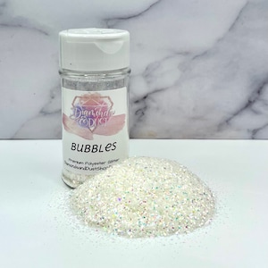 May include: A clear plastic jar filled with white iridescent glitter. The jar has a white lid and a label that says "Diamonds & Dust" and "Bubbles Premium Polyester Glitter DiamondsandDustShop.com".