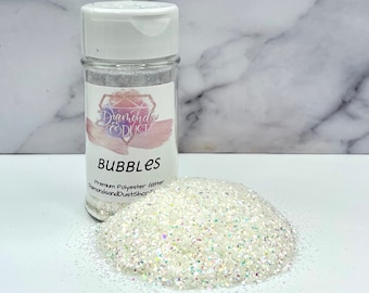 May include: A clear plastic jar filled with white iridescent glitter. The jar has a white lid and a label that says "Diamonds & Dust" and "Bubbles Premium Polyester Glitter DiamondsandDustShop.com".