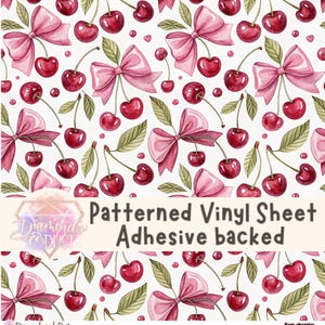 Könnte beinhalten: Gemusterte Vinylfolie mit Kleberückseite. Das Design zeigt Aquarellkirschen und rosa Schleifen auf weißem Hintergrund. Der Text auf dem Bogen lautet "Patterned Vinyl Sheet Adhesive backed".