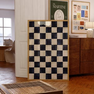 Puede incluir: Una impresión enmarcada con un patrón de tablero de ajedrez en blanco y negro con un marco de madera. La impresión está colgada en una pared en una habitación con un suelo de madera y una cómoda de madera.